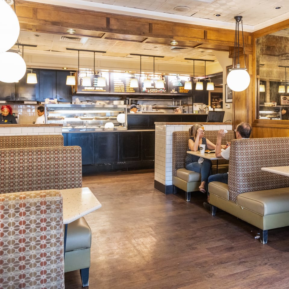 Restaurant interior with customers dining in booths and staff working behind a service counter.