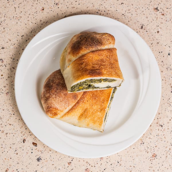 Golden-brown calzone, sliced to show spinach and cheese filling, on a white plate.