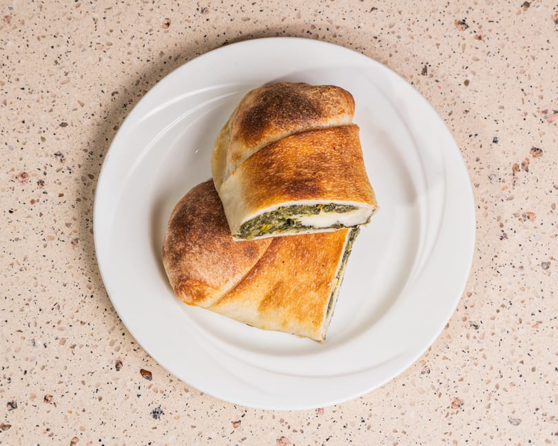 Golden-brown calzone, sliced to show spinach and cheese filling, on a white plate.