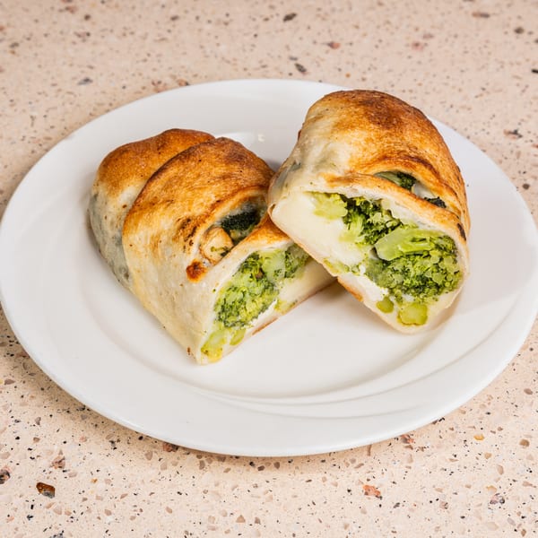 Golden-brown stromboli halves revealing a vibrant broccoli and cheese filling on a white plate.