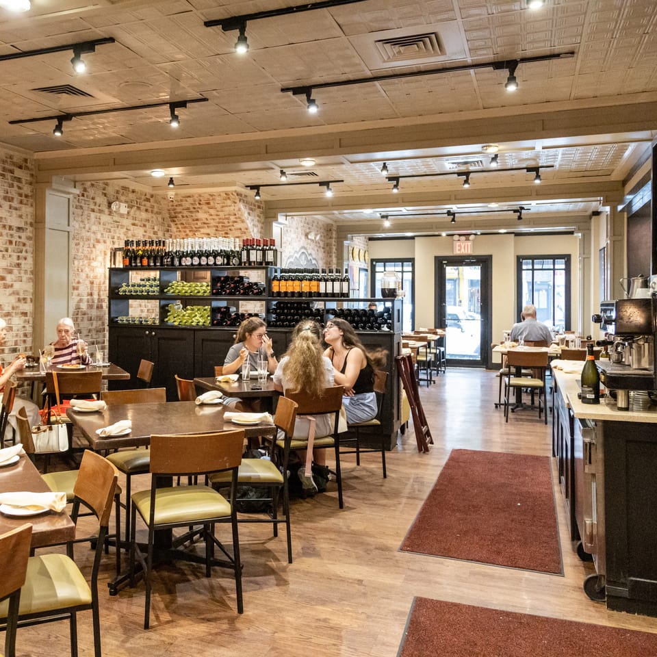 Cozy restaurant interior with brick walls, wooden tables, patrons dining, and a wine bottle display.