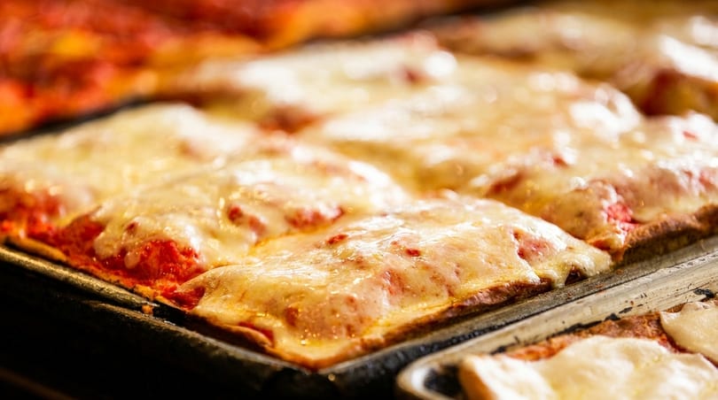 Close-up of freshly baked square-cut pizza slices with melted cheese and red sauce in a pan.