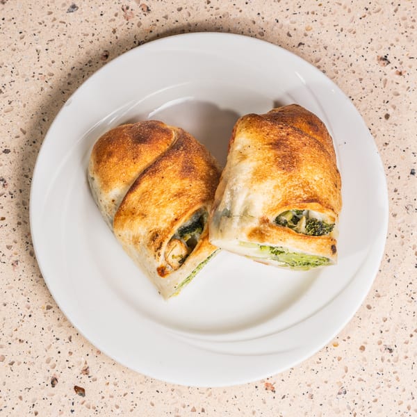 Two golden-brown pastries filled with broccoli and cheese on a white plate.