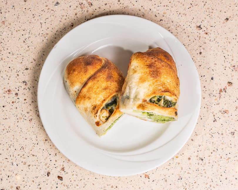 Two golden-brown pastries filled with broccoli and cheese on a white plate.