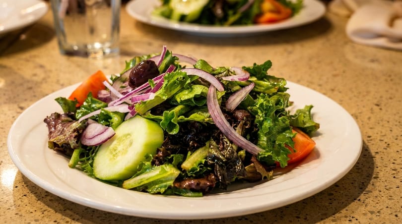 Fresh garden salad with lettuce, red onions, cucumbers, tomatoes, and olives on a white plate.