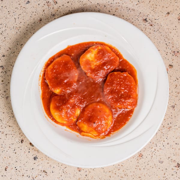 Five steaming ravioli in rich red tomato sauce on a white plate.