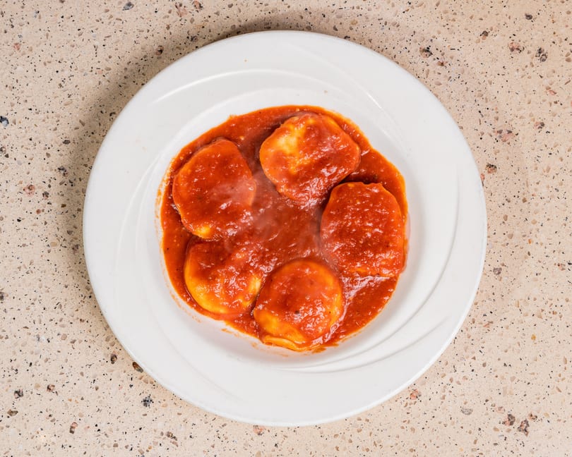 Five steaming ravioli in rich red tomato sauce on a white plate.