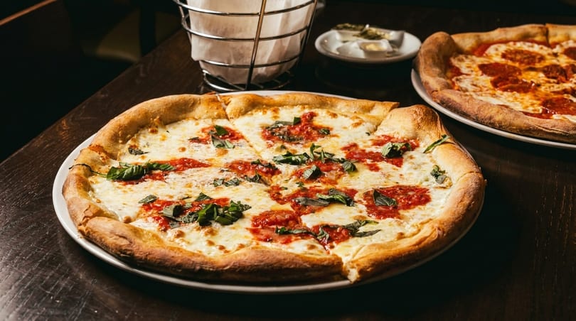 Two pizzas on a dark wooden table, one Margherita and one pepperoni, with napkins and butter.