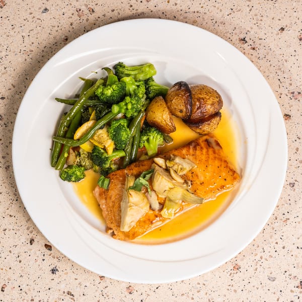 Glazed salmon with artichokes, roasted potatoes, broccoli, and green beans on a white plate.