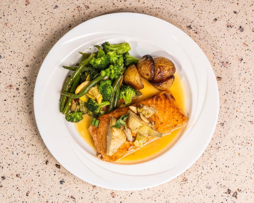 Glazed salmon with artichokes, roasted potatoes, broccoli, and green beans on a white plate.
