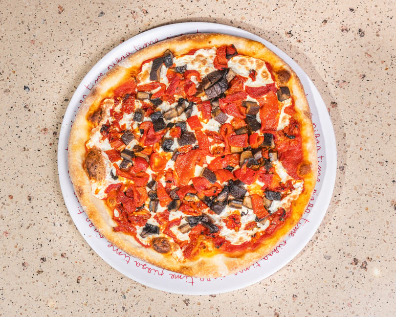 Round pizza with roasted red peppers, mushrooms, and mozzarella on a white 'pizza time' plate.