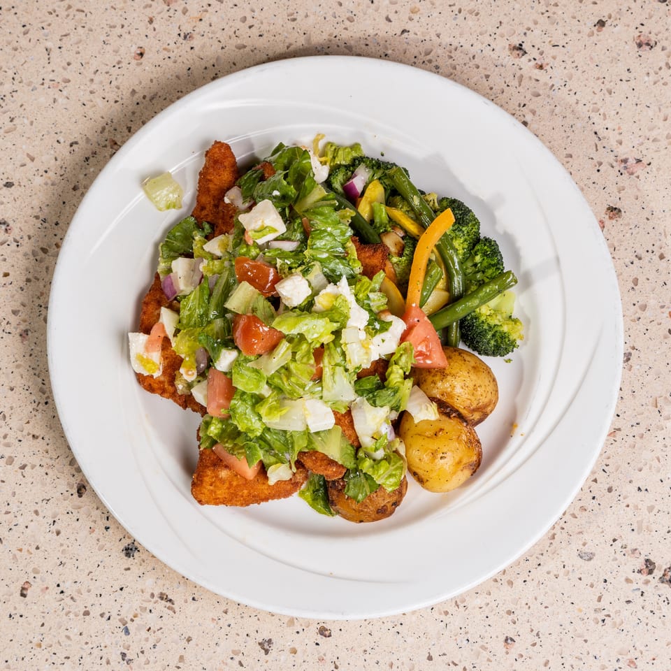 Fried chicken cutlets with a fresh salad, roasted potatoes, and steamed vegetables.