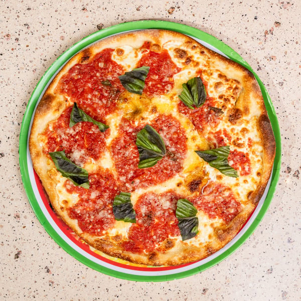 Margherita pizza with fresh basil on a green, white, and red striped plate.
