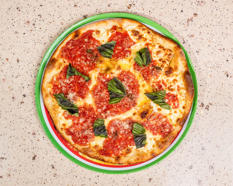 Margherita pizza with fresh basil on a green, white, and red striped plate.