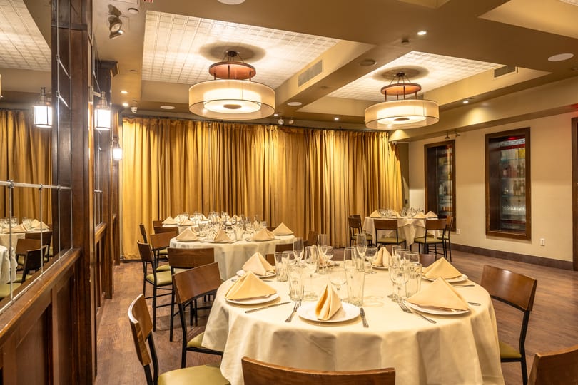 A private dining room with round tables set with white tablecloths, glasses, and napkins.