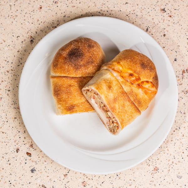 Two golden-brown calzones on a white plate, one cut open revealing cheese and meat filling.
