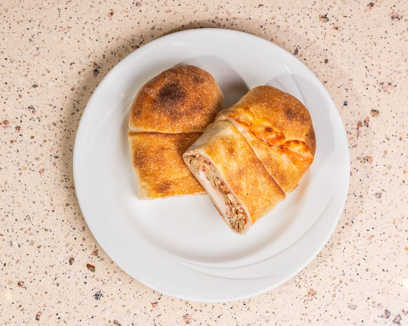 Two golden-brown calzones on a white plate, one cut open revealing cheese and meat filling.