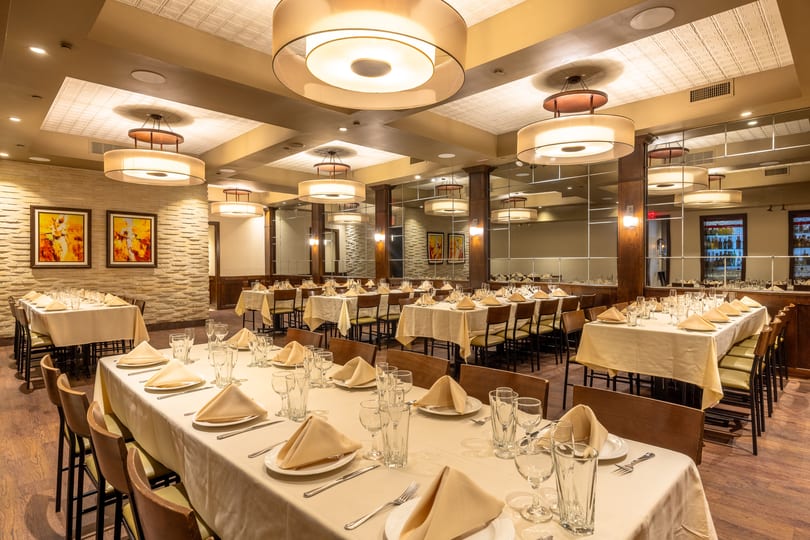 A large, elegant dining room with multiple long tables set with white tablecloths and place settings.