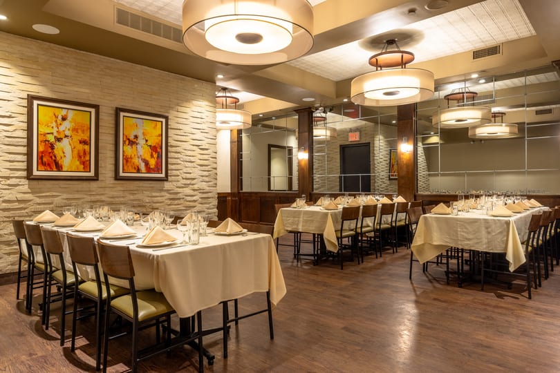Elegant dining room with set tables, modern art, and warm lighting, ready for guests.