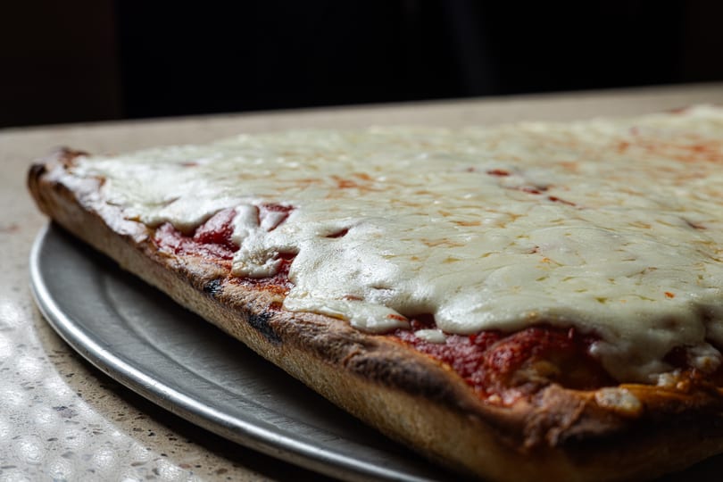 Close-up of a rectangular pizza with melted cheese and red sauce on a metal tray.
