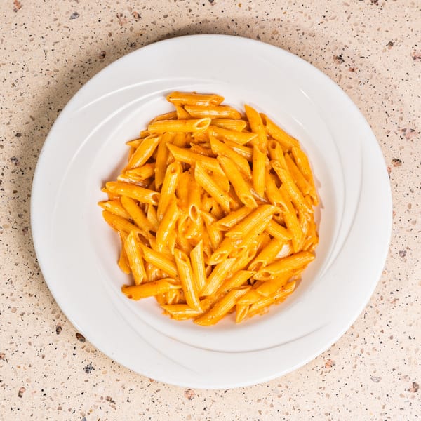 White plate filled with penne pasta in a creamy orange sauce on a speckled counter.