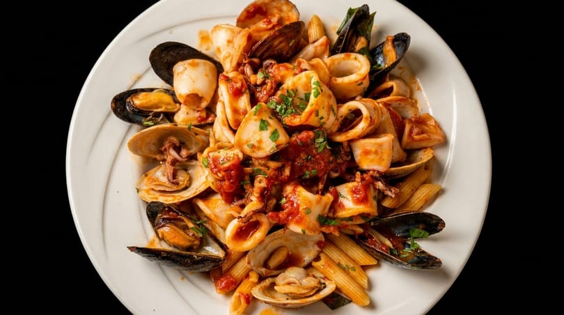 Seafood pasta with penne, mussels, clams, and calamari in a rich red sauce, garnished with parsley.